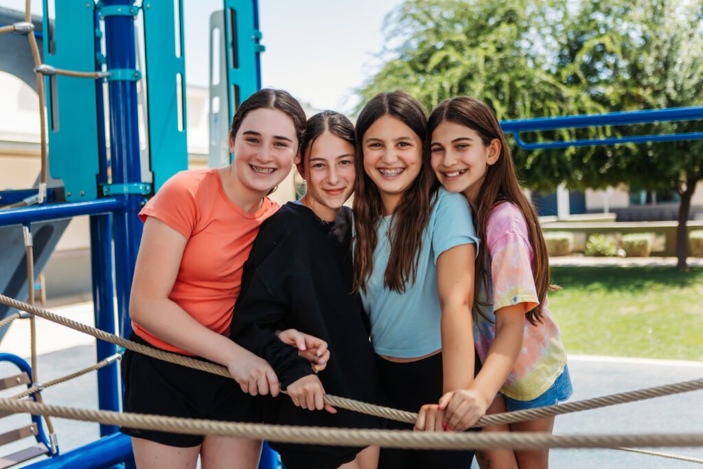 Four middle school girls standing close, smiling at the camera.